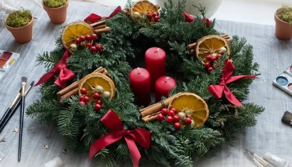 Advento vainikas iš eglišakių su raudonomis žvakėmis, džiovintais apelsinais ir cinamonu